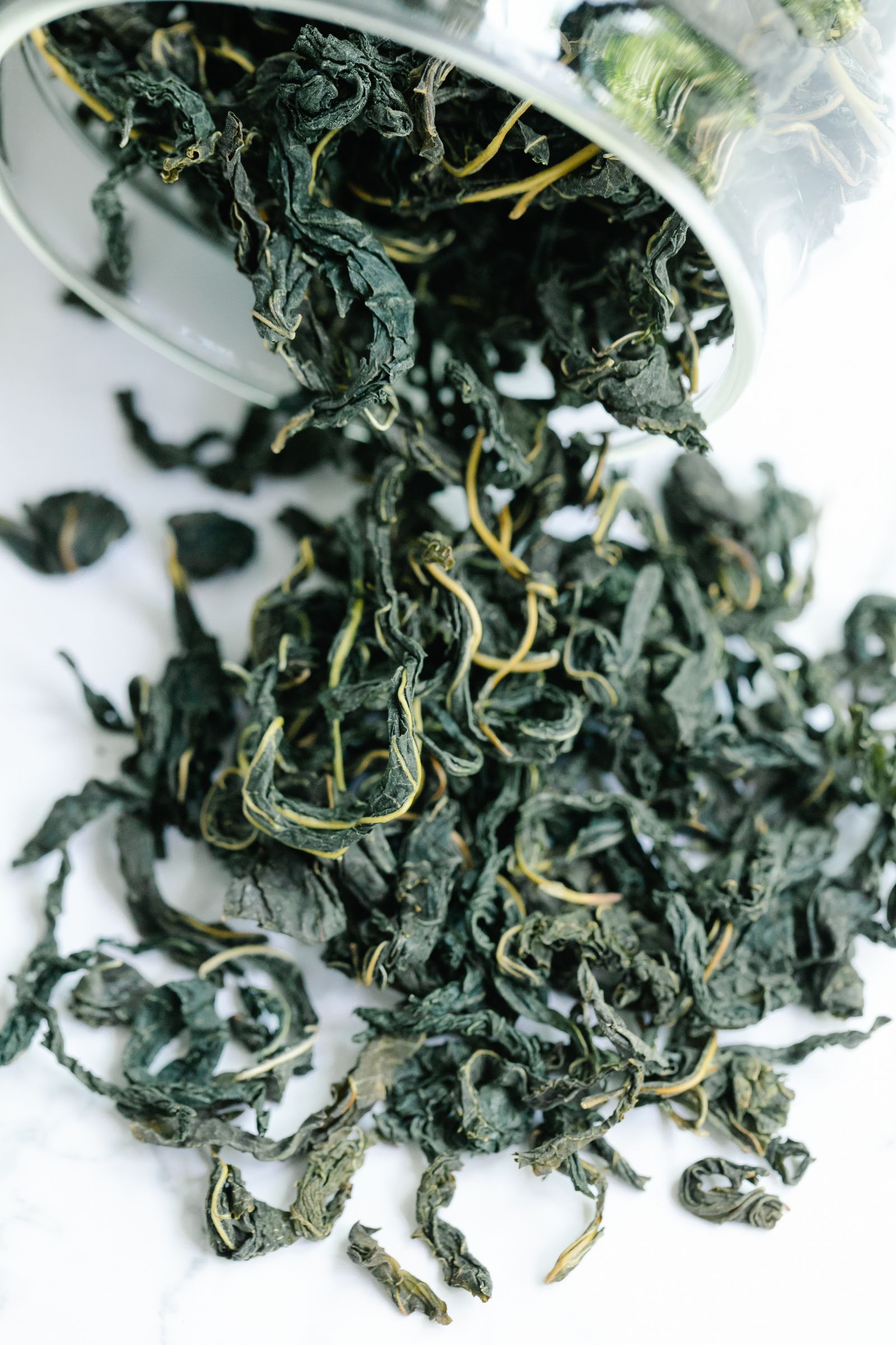 Dried sencha leaves tumbling from a jar — the thin, twisted needles that hours of rolling create