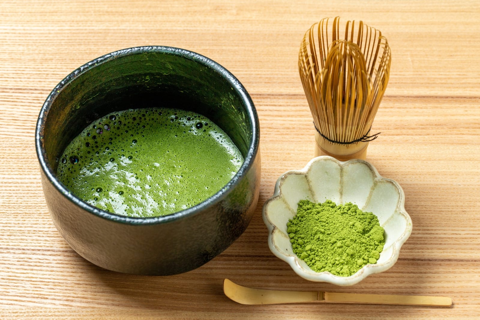 A bowl of freshly whisked matcha next to a small dish of bright green matcha powder