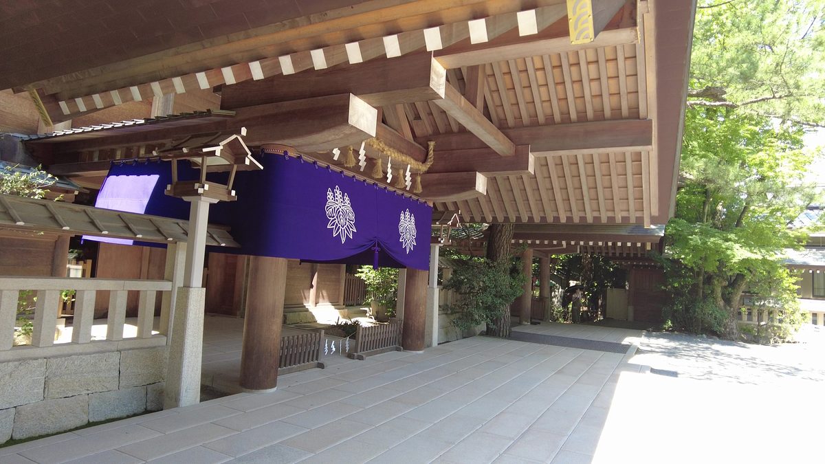 A shrine hall entrance draped with a purple curtain bearing white crests, beneath deep wooden eaves.