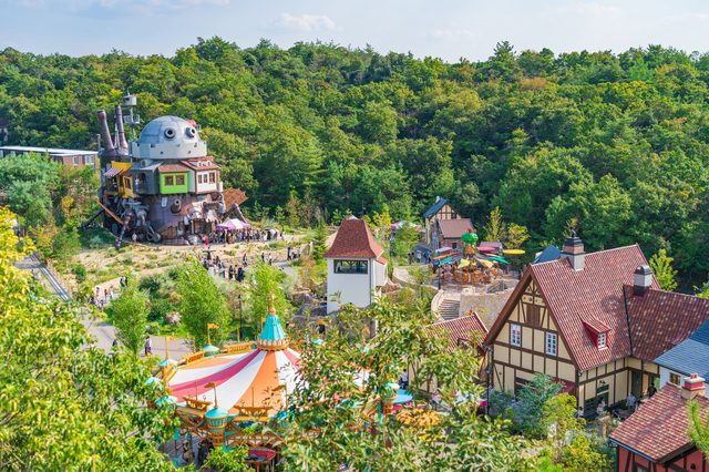 Hilltop view over the park — Howl's moving castle, colourful tents and storybook houses among the trees.