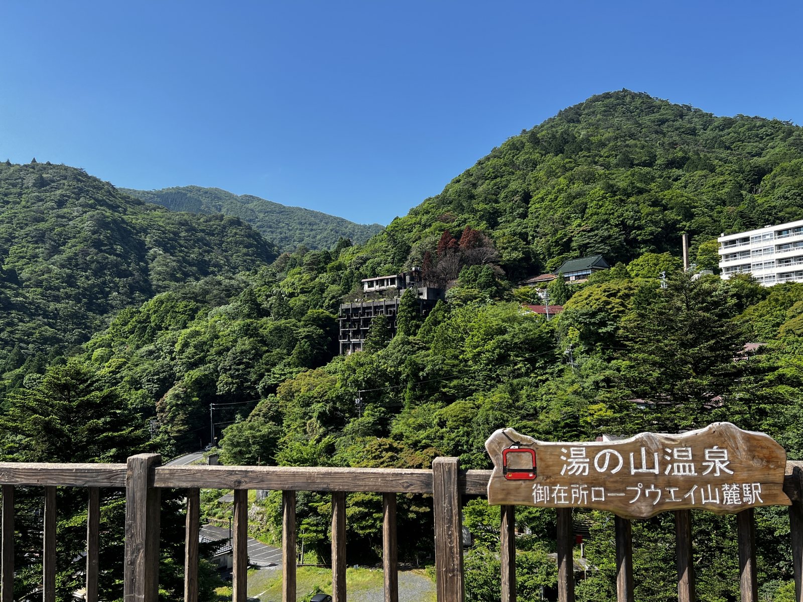 Yunoyama Onsen wrapped in summer green, with the Gozaisho Ropeway base-station signpost and inns along the slope.