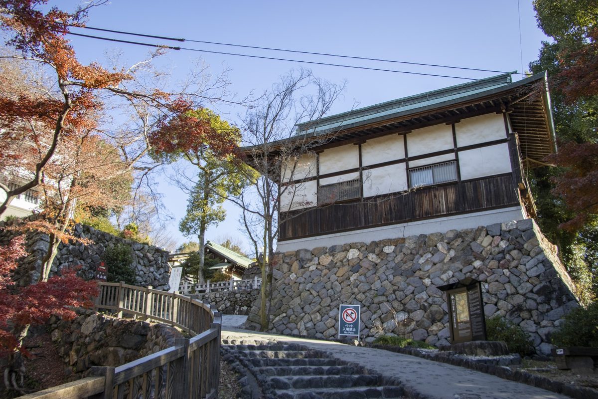 A timber castle building on a stone foundation, beside a curving path and bright autumn maple leaves.