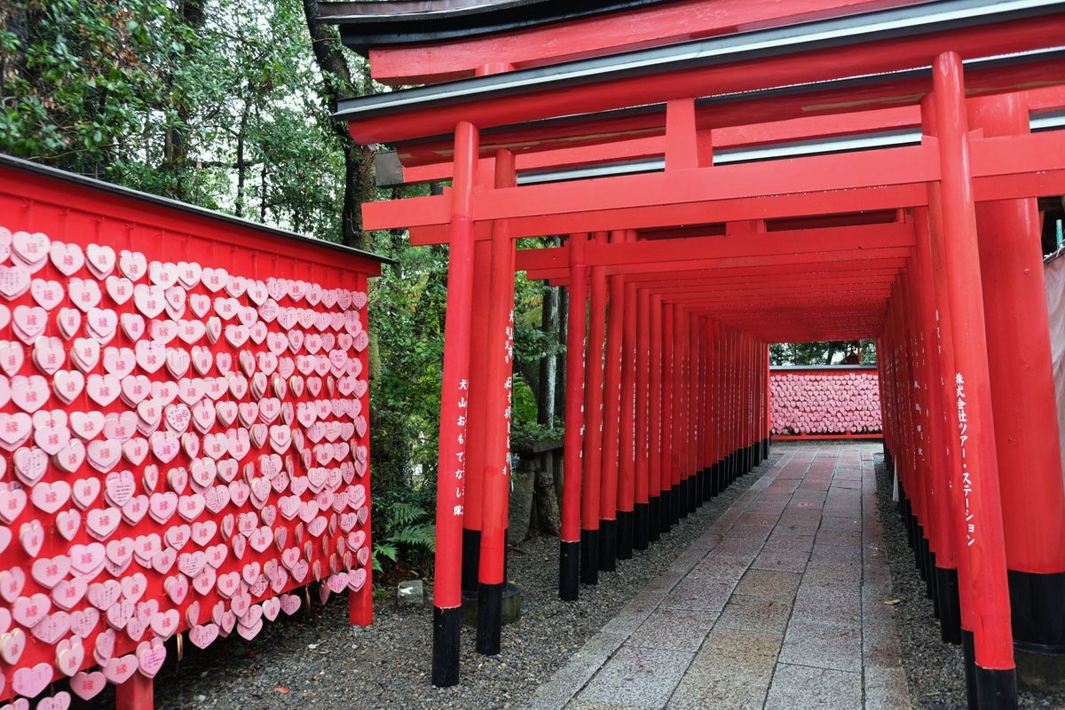 A tunnel of vermilion torii gates beside a wall covered in heart-shaped prayer plaques at Sanko Inari Shrine.