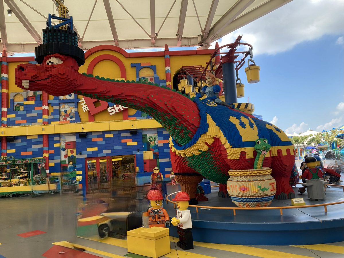 A giant LEGO dinosaur model standing outside one of the park shops