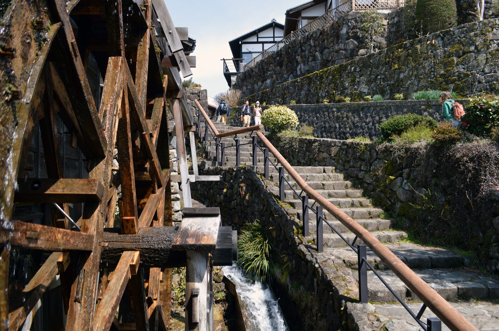 A wooden water wheel turning beside the old highway, surrounded by fresh green leaves