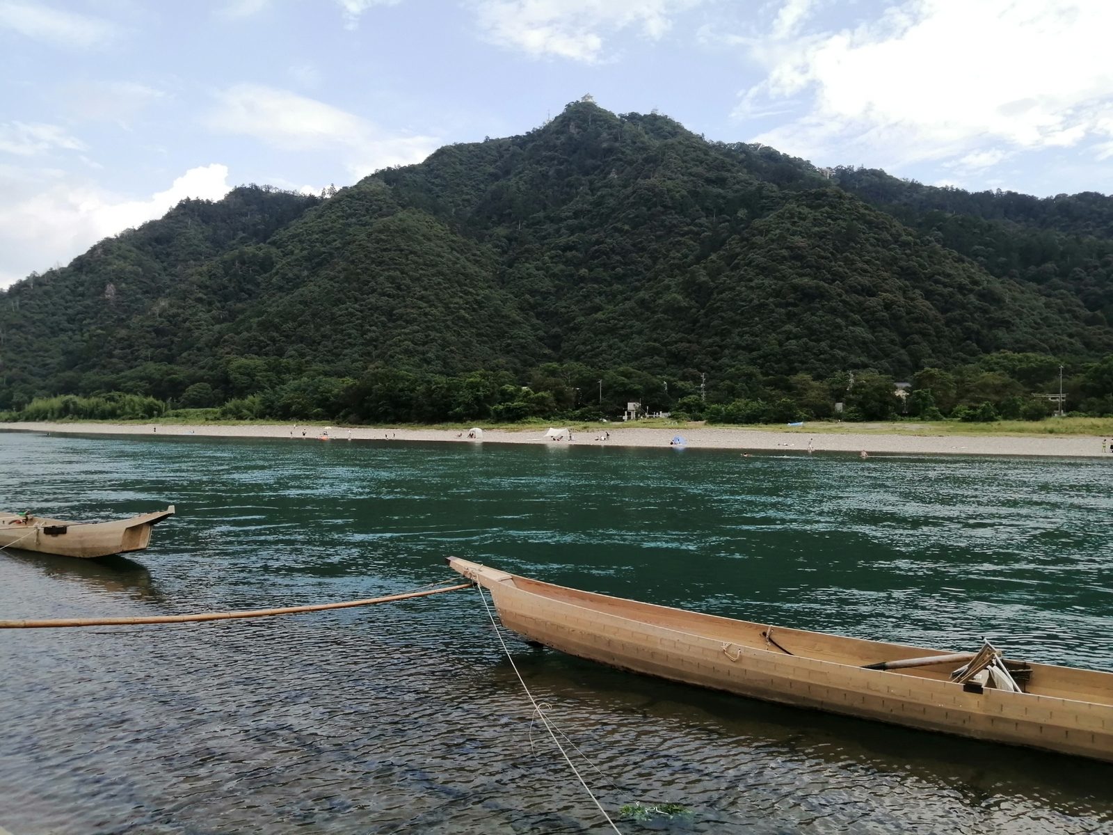 Cormorant boats moored on the Nagara River by day, below Mt. Kinka with Gifu Castle small on the wooded summit.