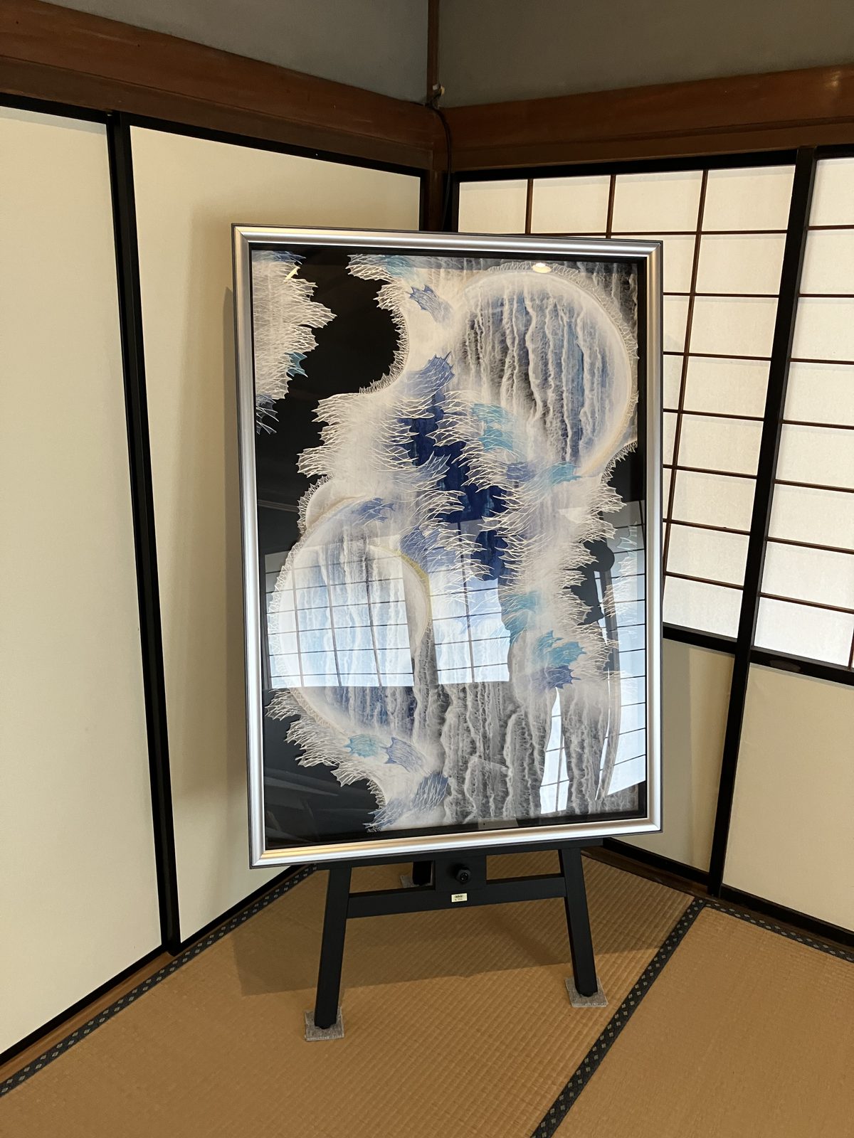 A framed washi artwork in soft blues and whites, displayed on an easel.