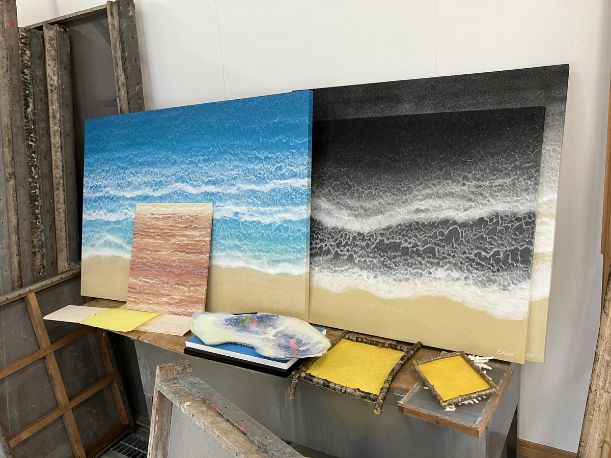 Finished wave-themed washi works beside small papermaking frames.