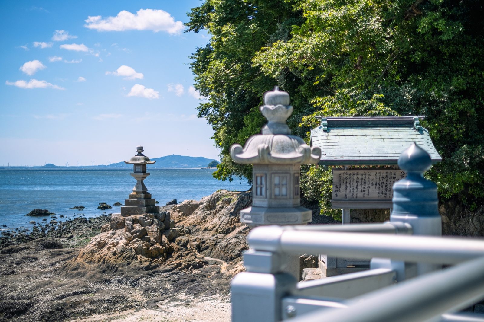 Stone lanterns on Takeshima's rocky shore, with Mikawa Bay beyond.