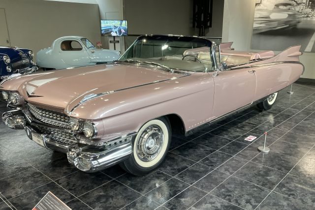 A pink 1950s American Cadillac convertible, all sweeping tail fins and whitewall tyres, on the polished gallery floor.