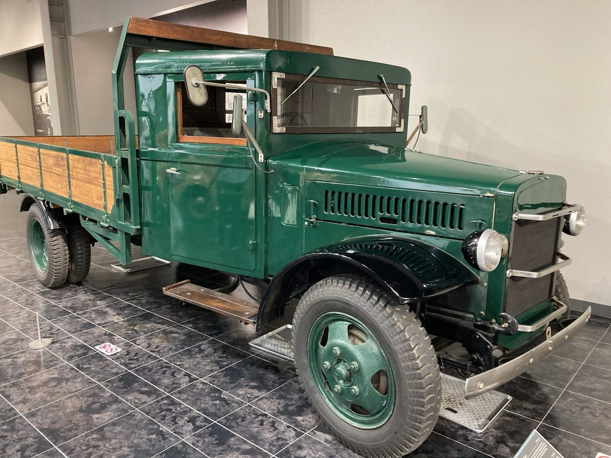 A green 1930s flatbed truck with a wooden cargo bed and a single round headlamp.