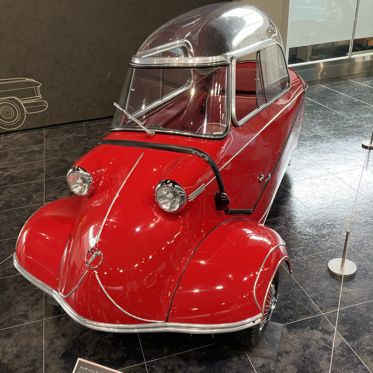 A tiny red Messerschmitt bubble car from Germany, with its clear bubble canopy and three wheels.