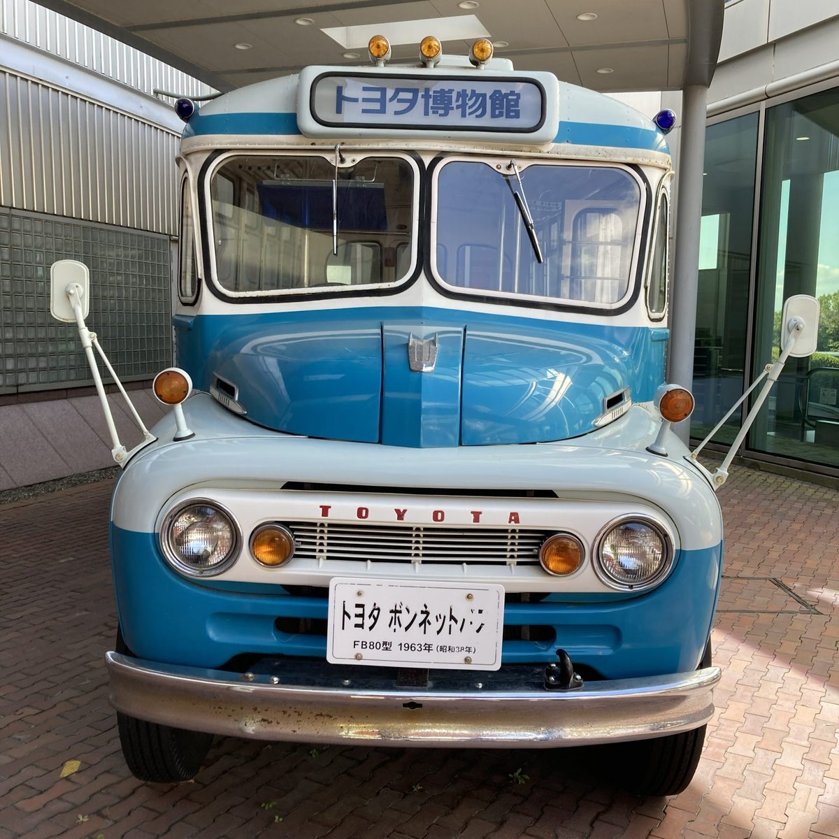 A blue-and-white 1963 Toyota bonnet bus (FB80) parked at the museum entrance.