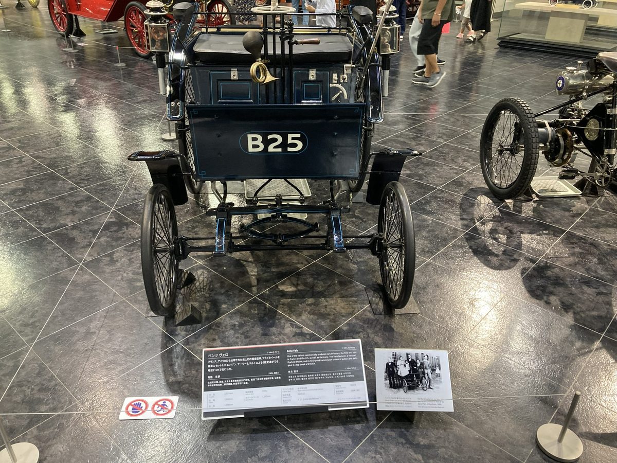 The back of an early horseless carriage marked B25, riding high on big spoked wheels.
