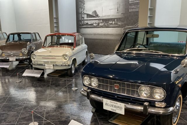 A line-up of 1960s Japanese classics, led by a navy 1965 Datsun Bluebird with a Mazda Carol alongside.